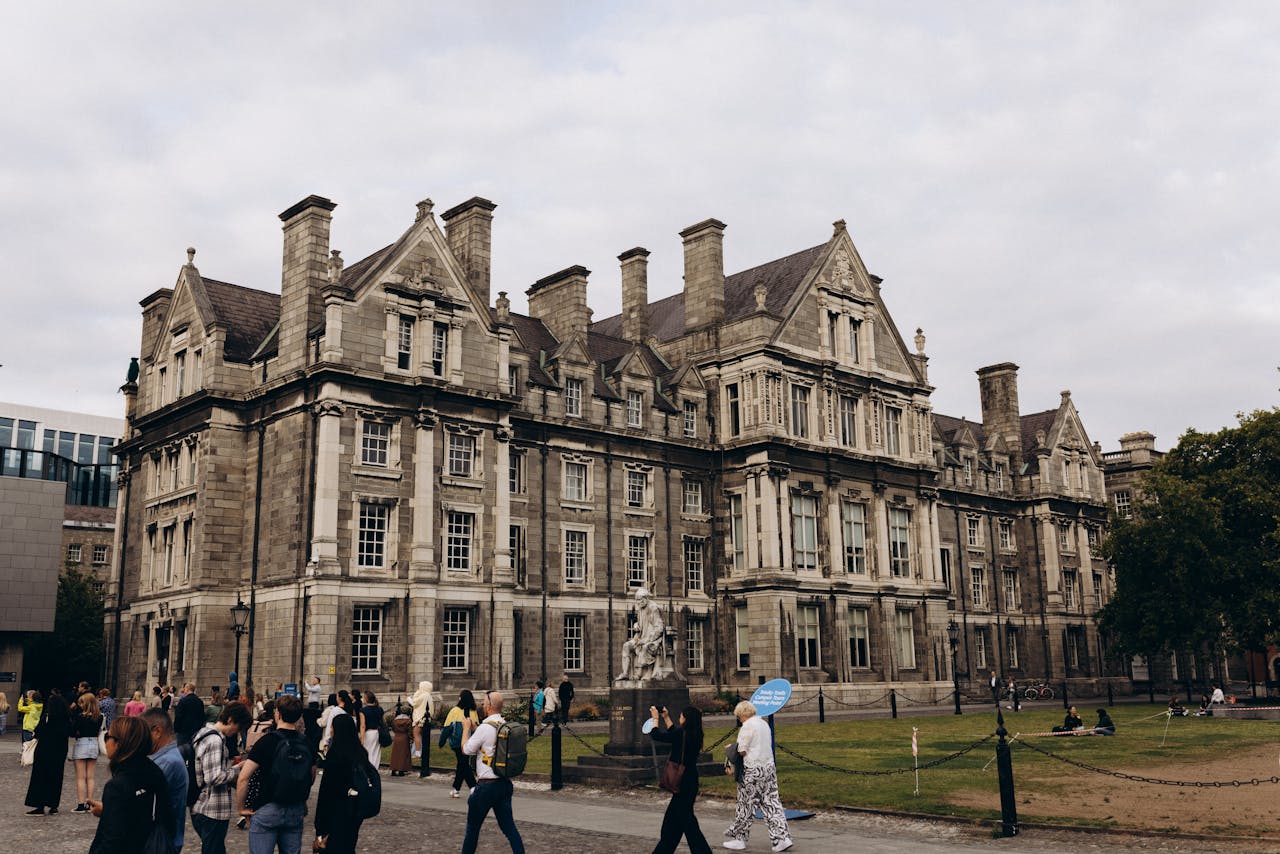 Historic architecture of Trinity College Dublin surrounded by visitors on a cloudy day.