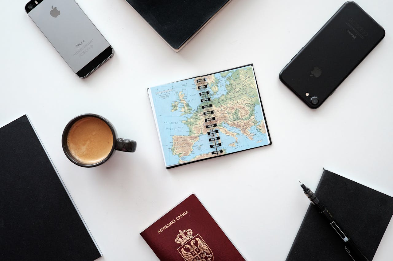 about-01 Flat lay of travel essentials with map, passport, and devices on a white surface.