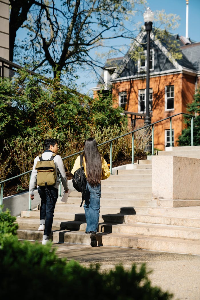 about-02 Two young adults walking up outdoor stairs surrounded by greenery and buildings.